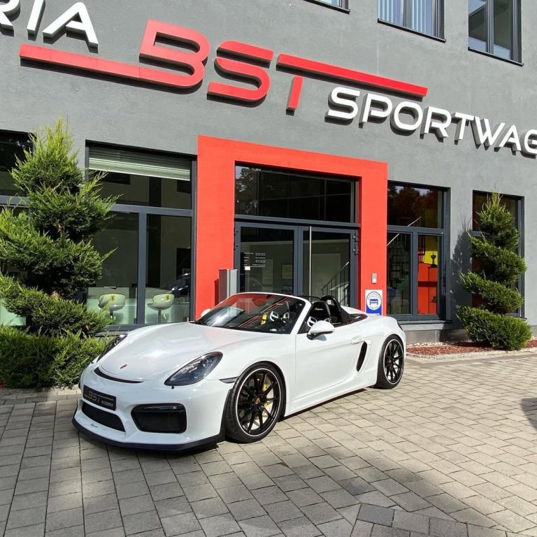 Weißer Sportwagen vor dem BST Sportwagen-Gebäude mit Pflanzen im Hintergrund.