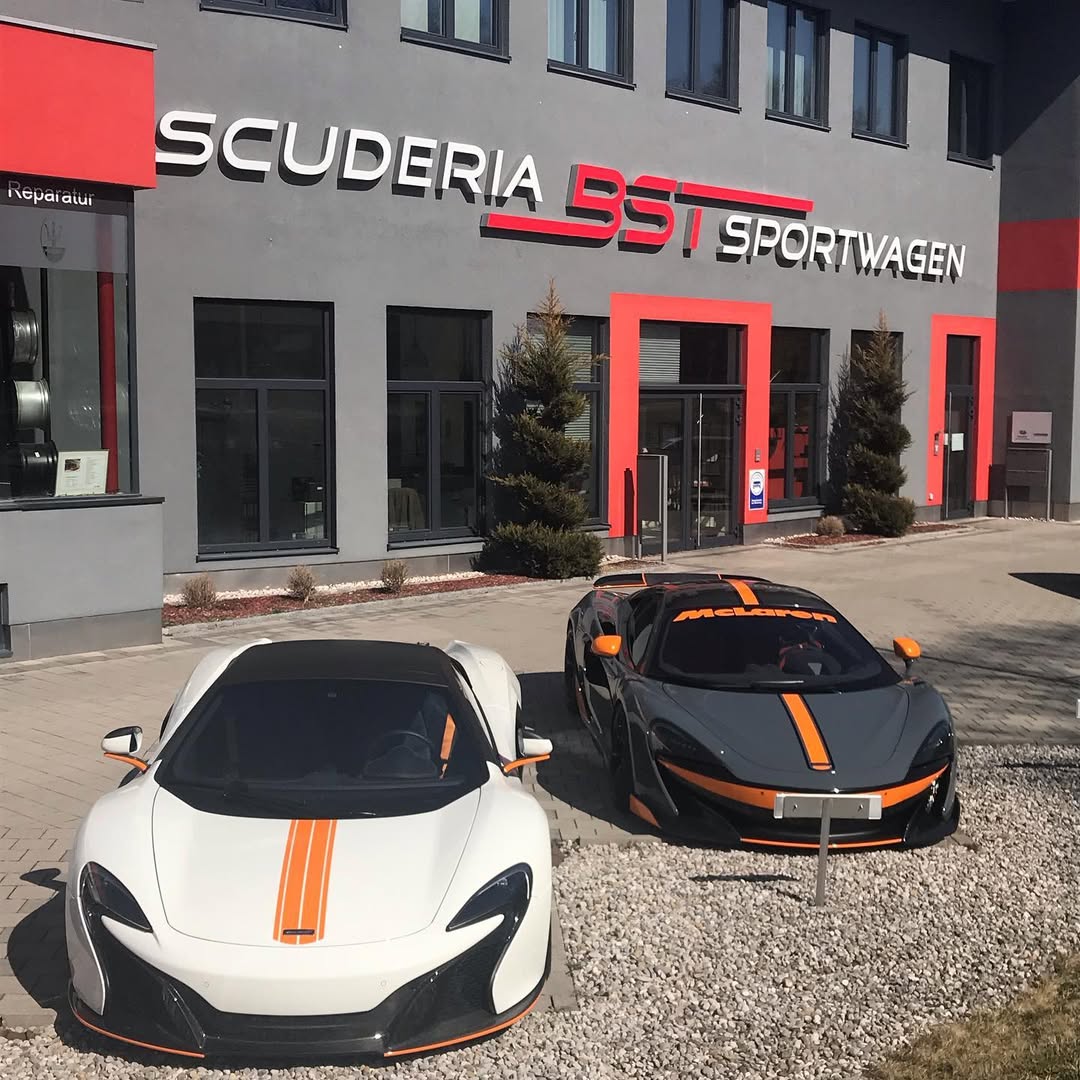 Zwei McLaren P1 Autos in der Einfahrt eines Sportwagenstudios mit modernem Gebäude.