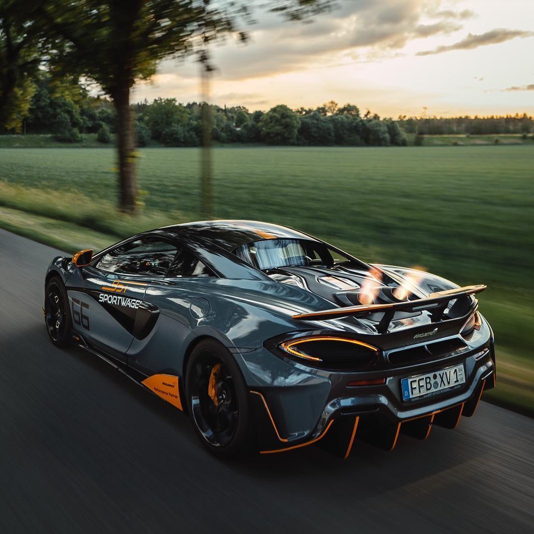 Ein grauer Sportwagen mit orangefarbenen Akzenten fährt entlang einer grünen Wiese.