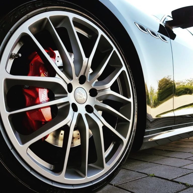 Sportlicher Autoreifen mit verchromtem Felgendesign und roten Bremssätteln.